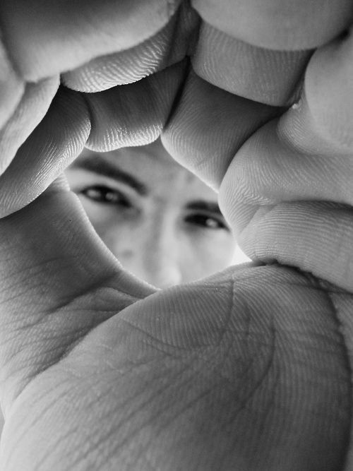 A photo of a man looking at a camera through his hands.